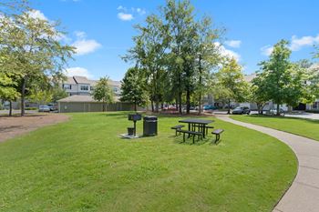A picnic area with a table and a trash can in the middle of a grassy area
